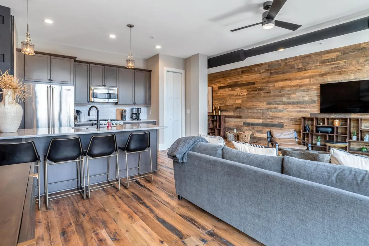 A cozy, contemporary kitchen and living space with a welcoming kitchen island, wood accent wall, comfortable seating area, and top-tier modern appliances. The open design encourages casual brunches, dinner parties, or unwinding after an evening out.