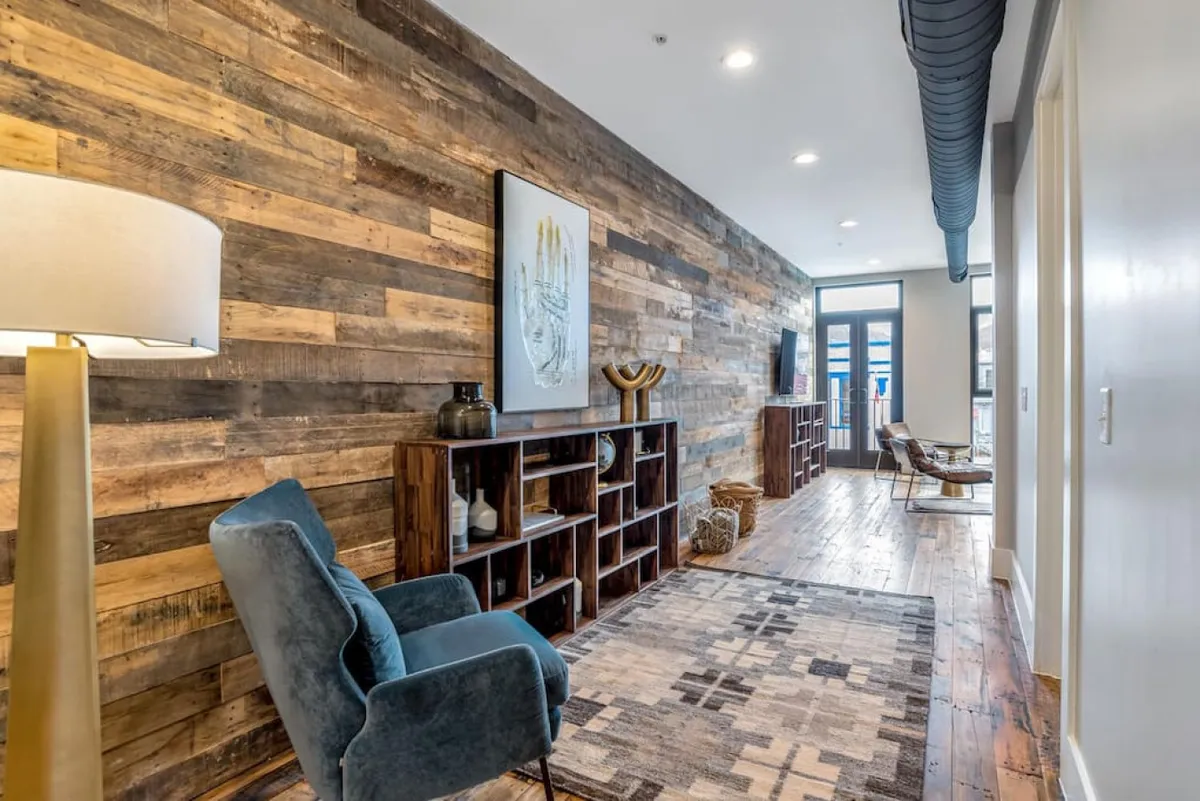 A thoughtfully designed reading nook with a blue upholstered chair, decorative shelving, wood accent wall, and curated artwork. The space is intimate yet modern, perfect for unwinding after an active day in the city.